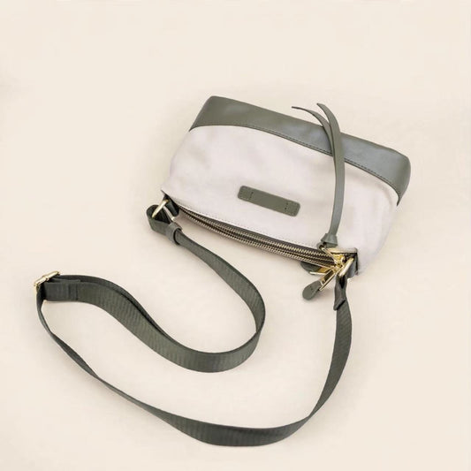 A small crossbody bag with a white body, dark gray top panel and strap, and gold-tone zipper hardware, photographed on a plain light beige background.
